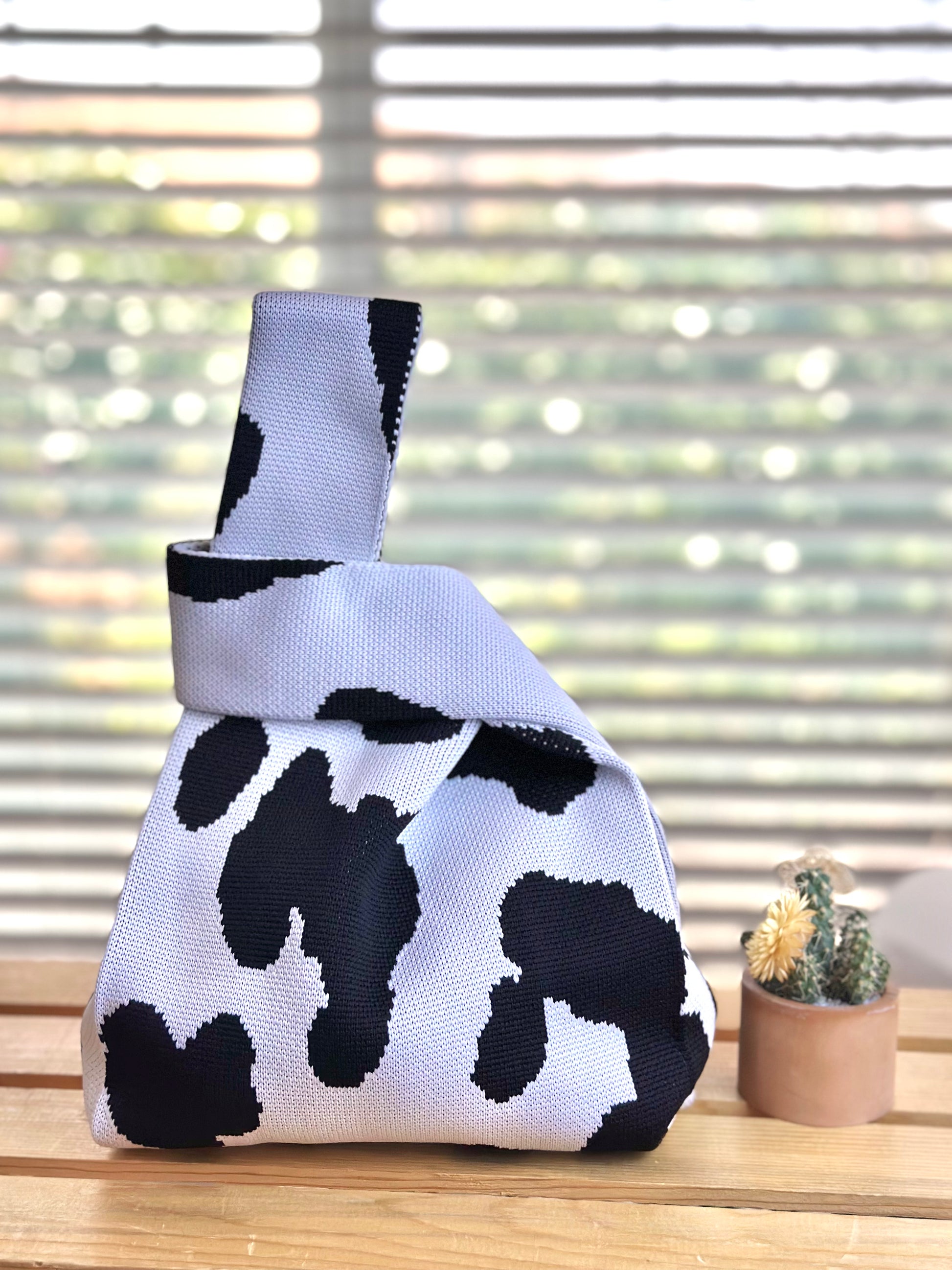 Cow print bag on a wooden surface with a blurred window background