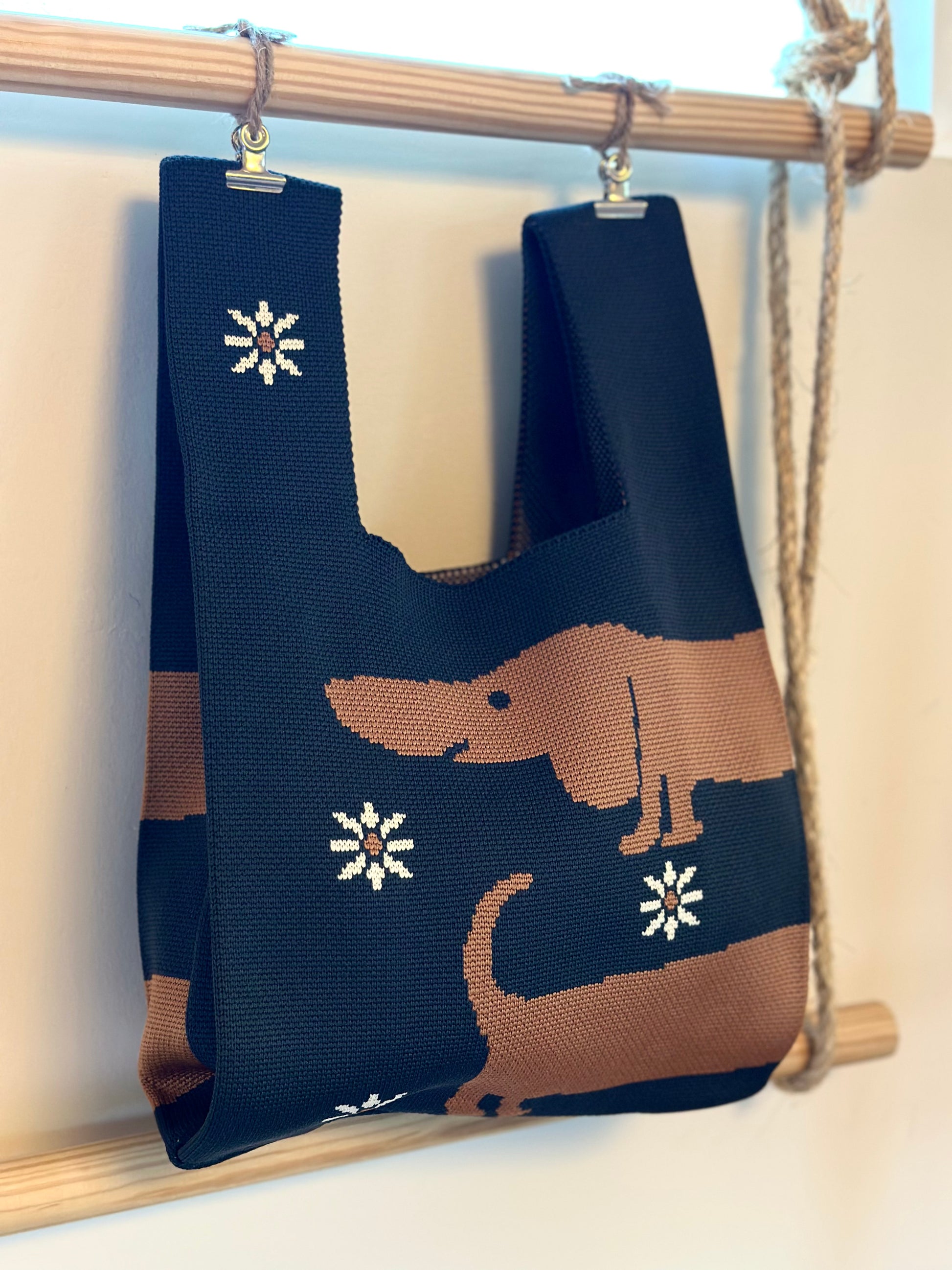 Navy blue tote bag with brown dog design and white snowflakes hanging on a wooden rod.