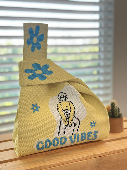 Yellow bag with floral designs and 'Good Vibes' text on a wooden surface.